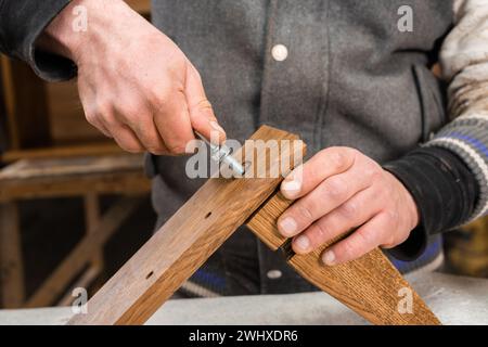 The carpenter screws a bolt into the leg of the cabinet closeup Stock Photo