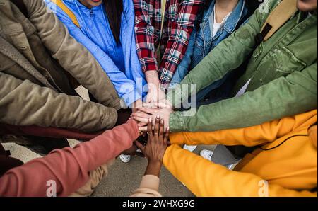 Diverse group of young friends stacking hands outdoors showing support and unity Stock Photo