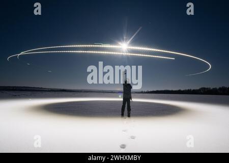 A man in a snowfield, the moon, footprints in the snow and a circle of light around at night Stock Photo