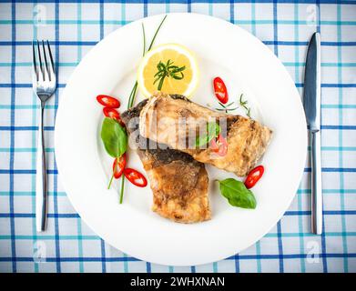 Fried fish on white plate and fork, knife Stock Photo