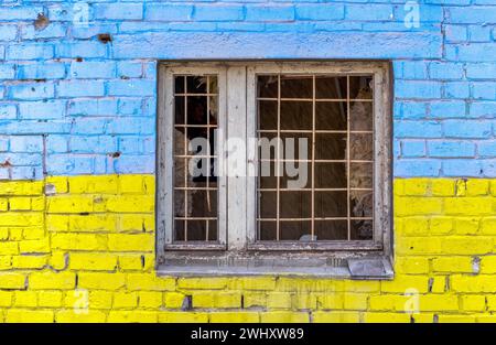 Pattern explosion damaged blue yellow house wall with window in Ukraine Stock Photo