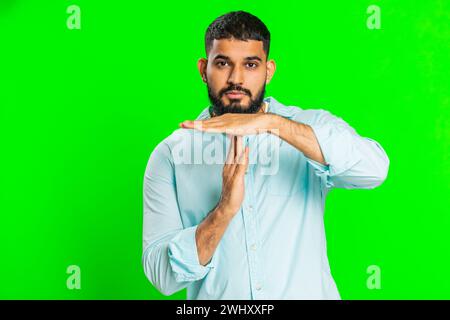 Tired serious upset Indian young man showing time out gesture, limit or stop sign, no pressure, I need more time, take a break, relax, rest, help. Arabian guy isolated on green chroma key background Stock Photo