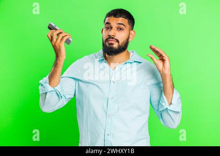 Disinterested Indian man having annoyed boring talk on smartphone. Arabian guy tired sleepy freelancer talking on mobile phone with friend, making online conversation on green chroma key background Stock Photo