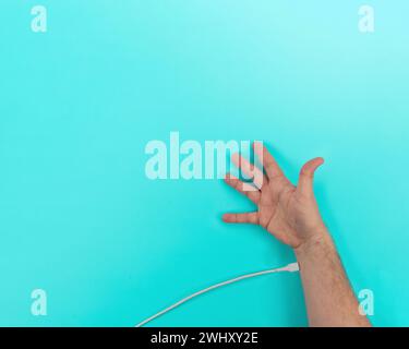 USB cable plugged into arm and hand concept blue background with copy space Stock Photo