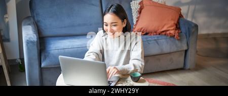 Beautiful asian girl works from home, studying with laptop, sitting in living room, being on remote, freelancing online Stock Photo