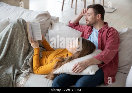Loving happy couple spending weekend together at home, reading and discussing interesting novel book Stock Photo