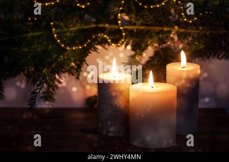 Three burning candles in front of dark fir branches with Christmas decoration and bokeh bubbles, seasonal holiday greeting card, Stock Photo