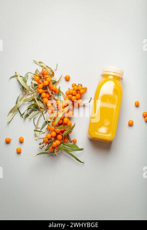 Sea buckthorn healthy juicy drink in bottle and branches with leaves and ripe berries top view on light grey simple background. Stock Photo