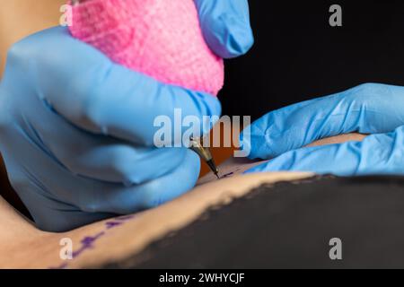 Needle tattoo machines inject a black ink into the skin of a woman. Tattoo art on body. Tattoo artist makes a tattoo woman on a Stock Photo