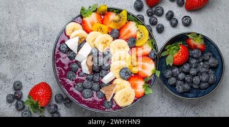 Healthy summer acai smoothie bowl with chia seeds, fresh banana, strawberry, blueberry, cocos, kiwi top view, rustic concrete ba Stock Photo