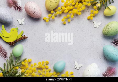 Decorative Easter composition featuring pastel-colored eggs, vibrant mimosa branches, and festive cutouts on a light, textured surface. Stock Photo