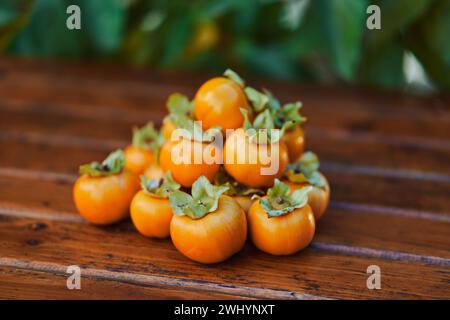 Bunch of ripe orange persimmons lies on a brown wooden table Stock Photo