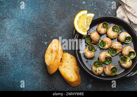 Escargots de Bourgogne Snails with Garlic Butter and Parsley in black cast iron pan with Lemon and Toasted Baguette Slices on ru Stock Photo