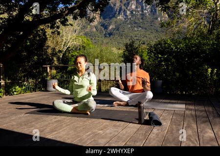 Happy diverse couple practicing yoga meditation sitting on deck in sunny garden, copy space Stock Photo