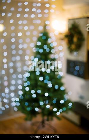 Green Christmas tree in the light of sparkling garlands in the room. Blur Stock Photo