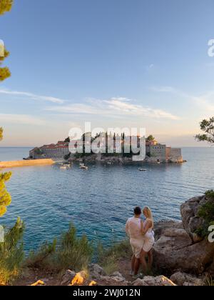 Budva, Montenegro - 01 august 2023: Man and woman stand hugging on the shore and look at the island of Sveti Stefan. Montenegro Stock Photo