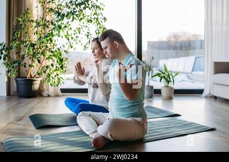 Young man with Down syndrome doing yoga at home with his mother on fitness ball. Workout routine for disabled man. Stock Photo