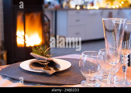 Serving festive table with plates, forks, knives, napkins, glasses close-up near stove fireplace in interior of loft house decor Stock Photo