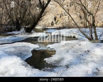 White ice and snow on frozen river, water flows below, winter background. Streams and rivers melting ice, springtime. Snow melting, flow. Stock Photo