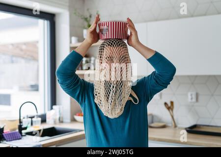 Portrait of young man with Down syndrome being funny, have mash net bag on head, holding popcorn bucket. Stock Photo