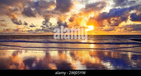 Sky with colorful clouds is reflected in the mudflat landscape at sunset, Norderney, Germany, Europe Stock Photo