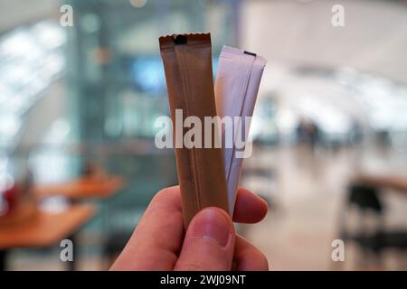 Close up left hand holding stick packets of brown and white sugar Stock Photo