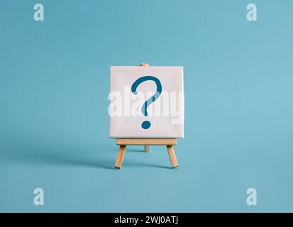 A canvas with question mark symbol on an easel with blue background. FAQ, confusion, uncertainty, to ask a question and query concepts. Stock Photo