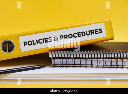 Policies and procedures written on the label of a yellow binder on the office desk. Business or company policies and procedures concept. Stock Photo