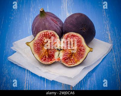 Three ripe figs on baking paper, blue wooden Stock Photo