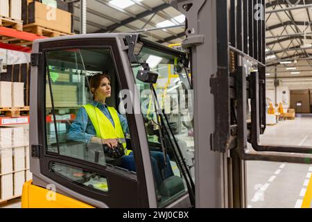 Female warehouse worker driving forklift. Warehouse worker preparing products for shipmennt, delivery, checking stock in warehouse. Stock Photo