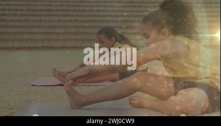 Image of bokeh lights over diverse schoolgirls exercising in outdoor yoga class Stock Photo