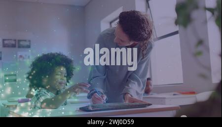 Image of light particles over happy diverse female teacher helping schoolboy at desk in class Stock Photo