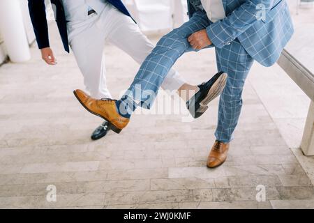 Groom and best man compete by showing their shoes on their outstretched legs. Cropped. Faceless Stock Photo