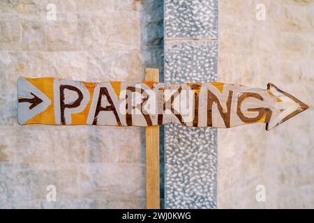 Wooden pointer with an arrow near the stone wall. Caption: Parking Stock Photo