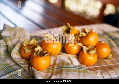 Ripe persimmon lies on a crumpled checkered tablecloth on a wooden table Stock Photo