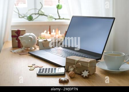 Christmas gifts, laptop and calculator on a decorated desk, economical holiday online shopping on a budget using discount offers Stock Photo
