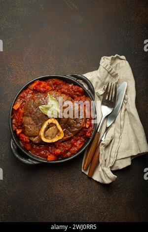 Traditional Italian dish Ossobuco all Milanese made with cut veal shank meat with vegetable tomato sauce served in black cassero Stock Photo