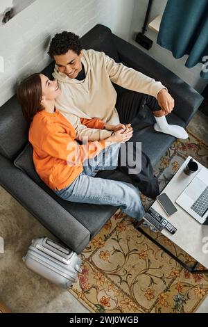 Loving couple enjoys a calm moment while relaxing on sofa with a smartphone, laptop and luggage Stock Photo