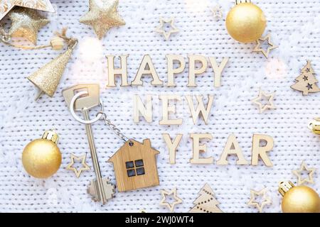 House key with keychain cottage on festive knitted background with stars, lights of garlands. Happy New Year wooden letters, gre Stock Photo