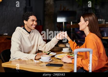 cheerful diverse couple enjoying a delicious meal in the charming indoor restaurant, holding hands Stock Photo
