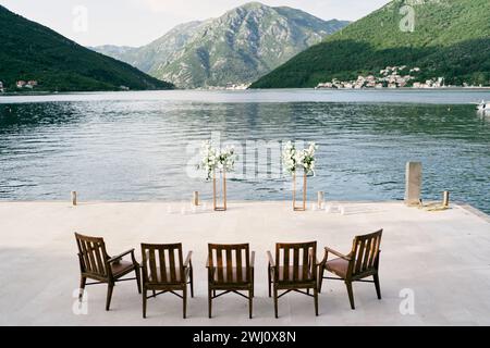 Wooden chairs stand in a row in front of a wedding semi-arch on a pier by the sea Stock Photo