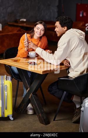black man and happy woman using smartphone while sitting at table with coffee in cafe Stock Photo