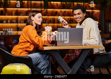 happy diverse couple looking at laptop in a modern cafe, woman holding coffee cup near black man Stock Photo