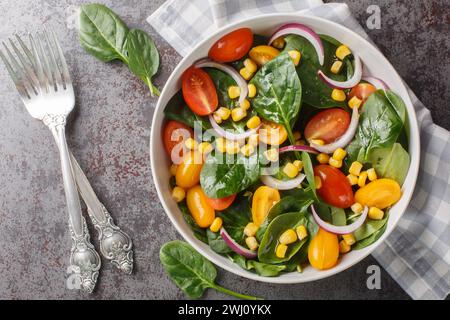 Light simple salad of fresh spinach, corn, cherry tomatoes and red onions with olive oil dressing close up in a bowl on the table. Horizontal top view Stock Photo