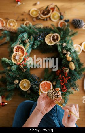 Decorator paints a fir cone with gold while sitting near the Christmas wreath. Cropped. Top view Stock Photo