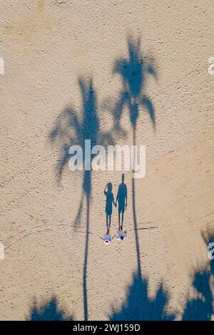 Drone view from above at a couple of men and woman walking on the beach with palm trees Stock Photo