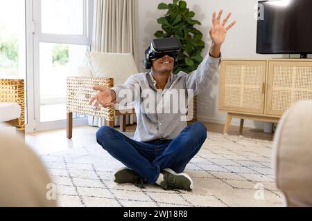 Happy biracial man using vr headset touching virtual screen at home Stock Photo