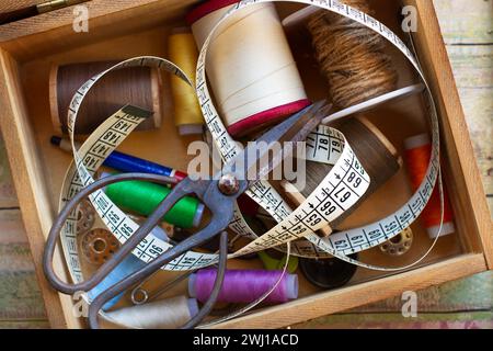 Thread, scissors and a measuring tape in a wooden box on a wooden table in a top view Stock Photo