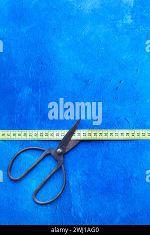 Scissors with large handles cutting a measuring tape on a blue background with copy space Stock Photo