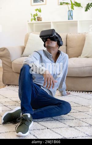 Biracial man using vr headset sitting on floor at home Stock Photo